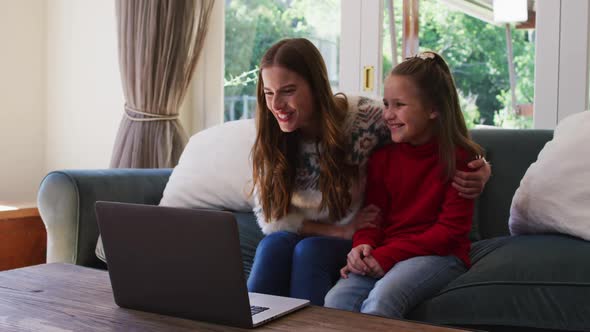 Caucasian woman and daughter smiling while having a video call on laptop sitting on the couch at hom