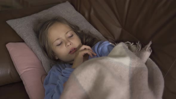 Young Caucasian Girl in Blue Sweater Laying Under the Warm Blanket and Taking Temperature. Close-up