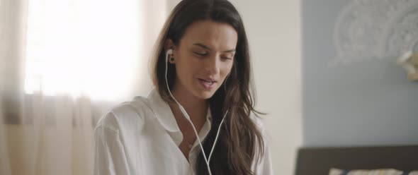 Close up of a young woman talking to someone through earphones while sitting on bed