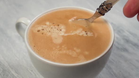 Person hand stirring coffee with spoon in white cup 