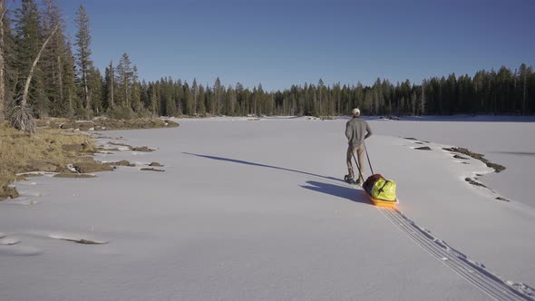 Man pulling his sled in the snow while adventuring through the woods.