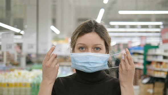 A Young Woman Puts on a Medical Mask in a Grocery Supermarket Close Up