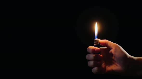 Hand Ignites Flames on Lighter on Black Background