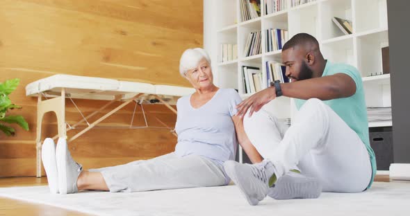 Video of african american male physiotherapist exercising with caucasian senior woman