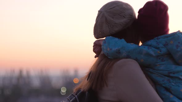 Mother and daughter standing on evening city lanscape. A little girl hugging and kissing mom