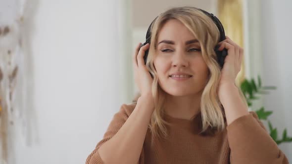Portrait of young happy woman in headphone dancing at home in bright room