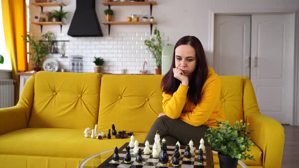 Young Woman Sitting on Yellow Sofa and Playing Chess in Room