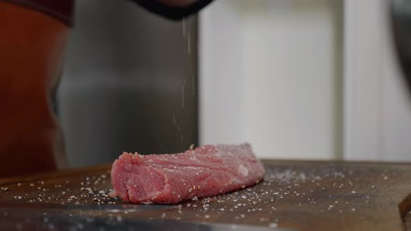 Chef applying pepper on raw piece of steak.