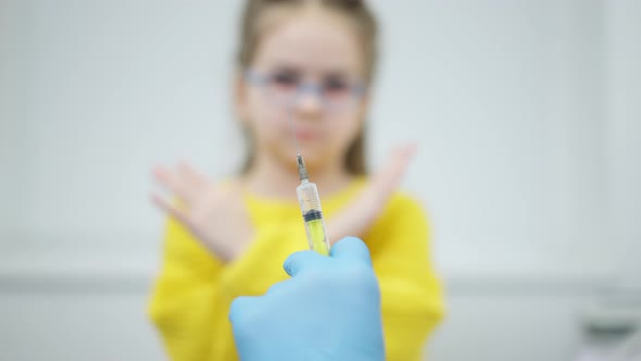 Closeup of Pediatrician Hand Holding Syringe with Covid Vaccine and Blurred Caucasian Little Girl