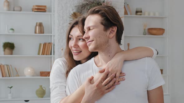 Caucasian Happy Couple Loving Husband and Wife Embracing Stand at Home Looking Out Window