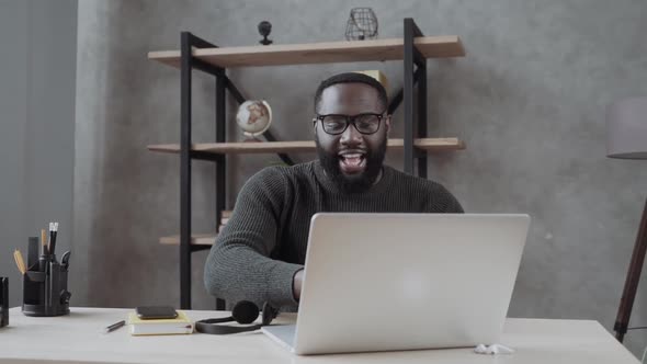 Happy African Millennial Guy Sitting at Table Look at Laptop Screen Feels Excited Received Great