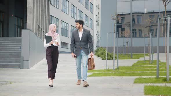 Smiling Woman in Hijab Carrying Clipboard and Coffee While Walking Near Office