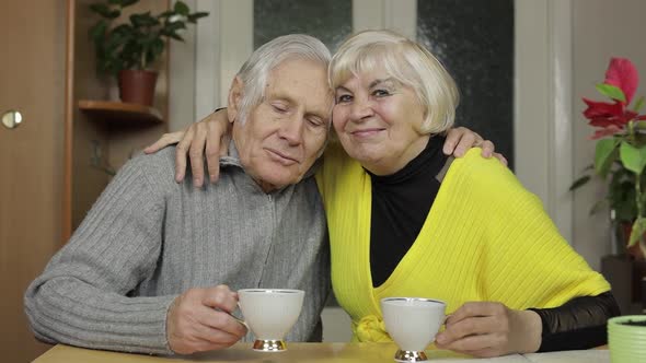 Happy Old Grandparents Couple Sit on Table at Home Enjoy Drinking Tea Together