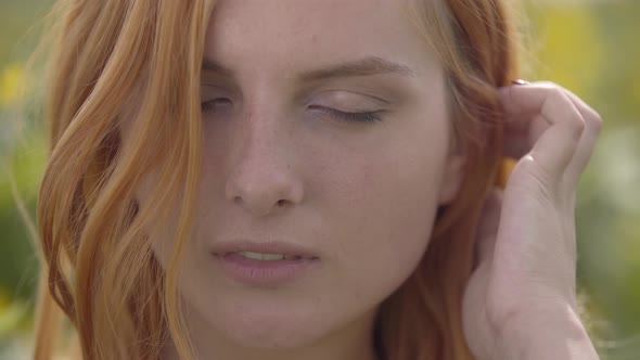 Close-up Face of Confident Sensual Girl with Red Hair and Green Eyes Standing on Sunflower Field