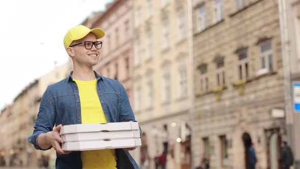 A Young Happy Delivery Man is Making Delivery of Three Pizzas