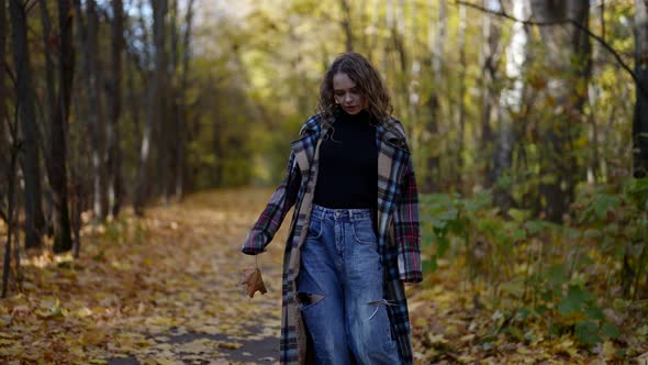 Lonely Woman in Check Coat is Walking in Forest in Autumn Kicking Fallen Foliage