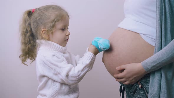 Girl Puts Blue Baby Booties on Palms with Pregnant Mommy