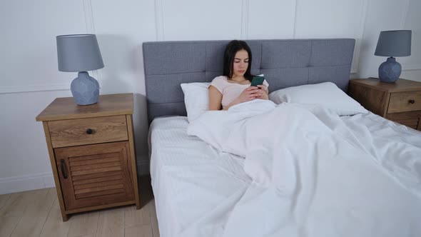 Young Girl Lies In Bed With Smartphone