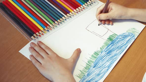 Childrens Hands Closeup Draw a House on the Lake with a Pencil