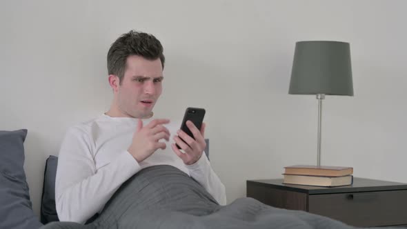 Man Reacting to Loss on Smartphone in Bed