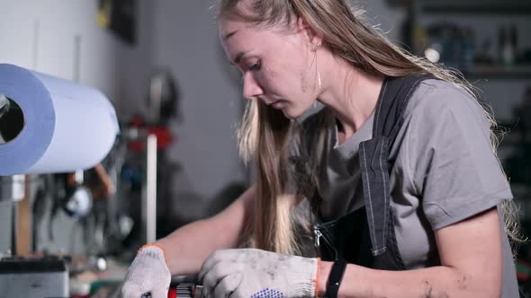 Side view of young woman repairing part of motorcycle engine in garage