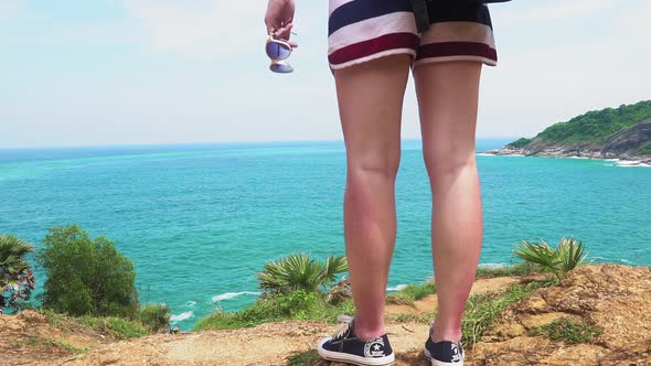 girl traveler's feet stand on the edge of a cliff by the sea of a tropical island