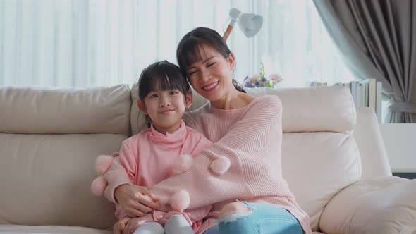 Portrait shot of lovely family Asian young little girl kid sit on sofa with mother in living room.