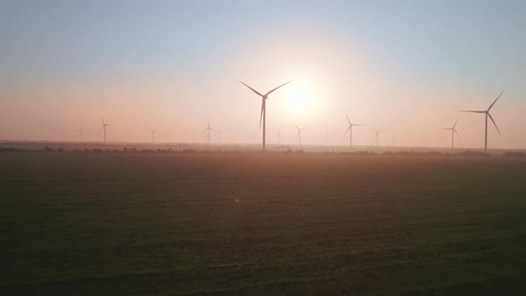 Windmills with rotating wings at sunset or sunrise.