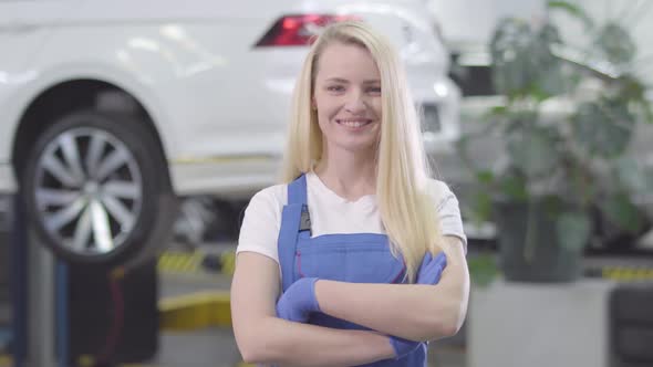 Portrait of Young Caucasian Woman Standing at the Background of White Car in Repair Shop. Blond