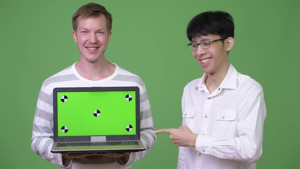 Two Young Multi-ethnic Businessmen Showing Laptop To the Camera While Pointing Finger