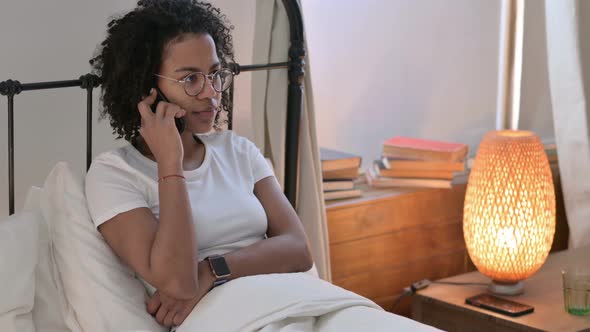 Young African Woman Talking on Smartphone in Bed 