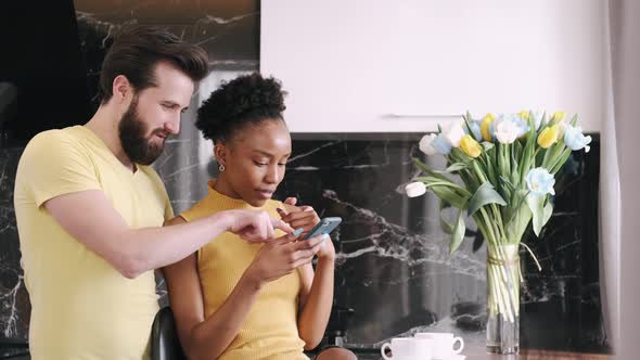 Multi Racial Couple Checking Something in Smartphone Standing in the Kitchen