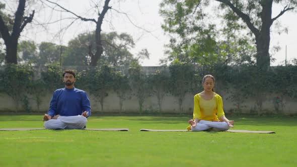 Lotus Yoga Pose or Padmasana is being done by an Indian couple in an Indian outfit