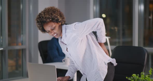 African Businesswoman with Pain in Back Holding Hand on Hip Standing Up From Office Chair