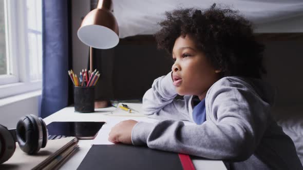 Mixed race girl sitting by desk looking through window