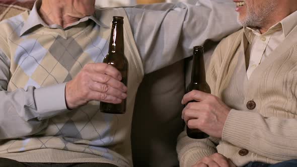 Two Pensioners Clinking Bottles Drinking Beer Sitting Sofa Together, Free Time