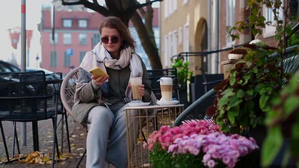 Tourist Woman in Sunglasses Drinks Hot Coffee in the Street Cafe of Old Town in Autumn 60p Slow