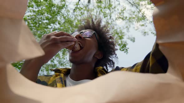 View From Inside Paper Bag of African Man Take Croissant and Bite Outdoors