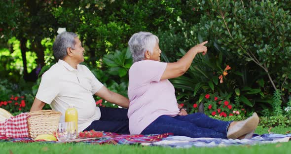 Video of happy biracial senior couple having picnic in garden