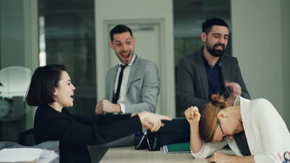 Cute Girls Office Workers Are Competing in Arm Wrestling Sitting in Room at Desk While Young Men in