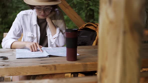 Young Girl In Hat A Tourist Sits In Campsite Resting Studying Map To Plan Further Progress A Tourist