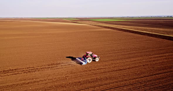 Drone shot of tractor seeding crop in plowed field