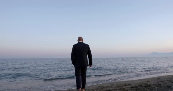 Barefoot Muscular Man in Black Suit Walks Along Sandy Beach