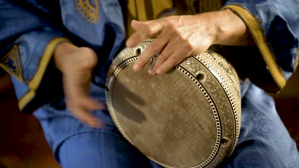 Tight shot of man in Moroccan dress playing arabic doumbek, darbuka, or derbeki