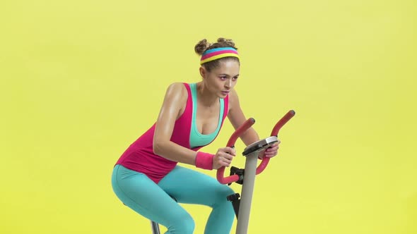 Portrait of Pleased Feminine Woman Wearing Colorful Sportswear Pedalling on Training Simulator in