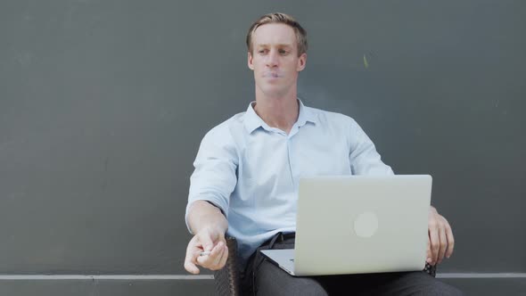 Man Sits with Modern Laptop and Smokes Cigarette Gray Wall on Background