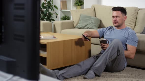 Man Sitting on Floor and Drinking Tea while Watching TV at Home