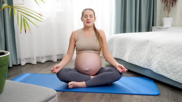 Beautiful Pregnant Woman Meditating and Practicing Yoga on Fitness Mat at Big Window at Home