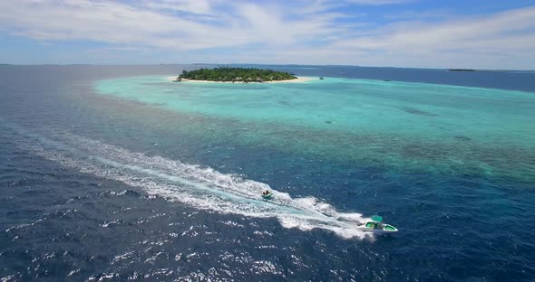 Aerial drone view of man and woman on an inflatable tube towing behind a boat to a tropical island