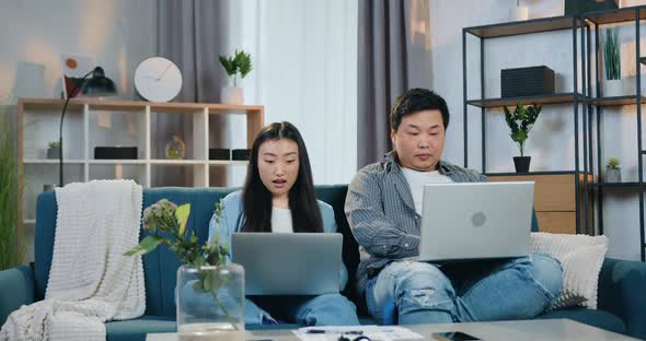 Asian Man and Woman Sitting on the Couch at Home and Raising Hands when Get Good News